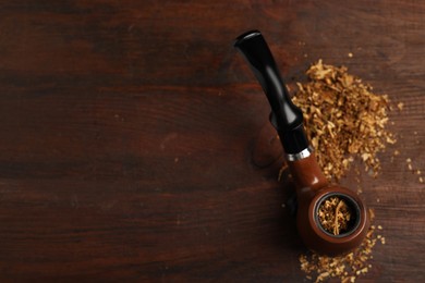 Photo of Smoking pipe with tobacco on wooden table, above view. Space for text