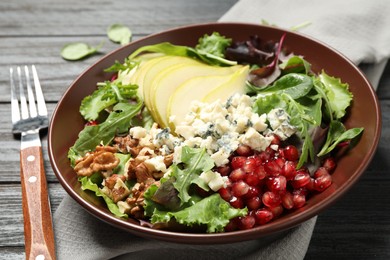 Photo of Tasty salad with pear slices and fork on black wooden table, closeup