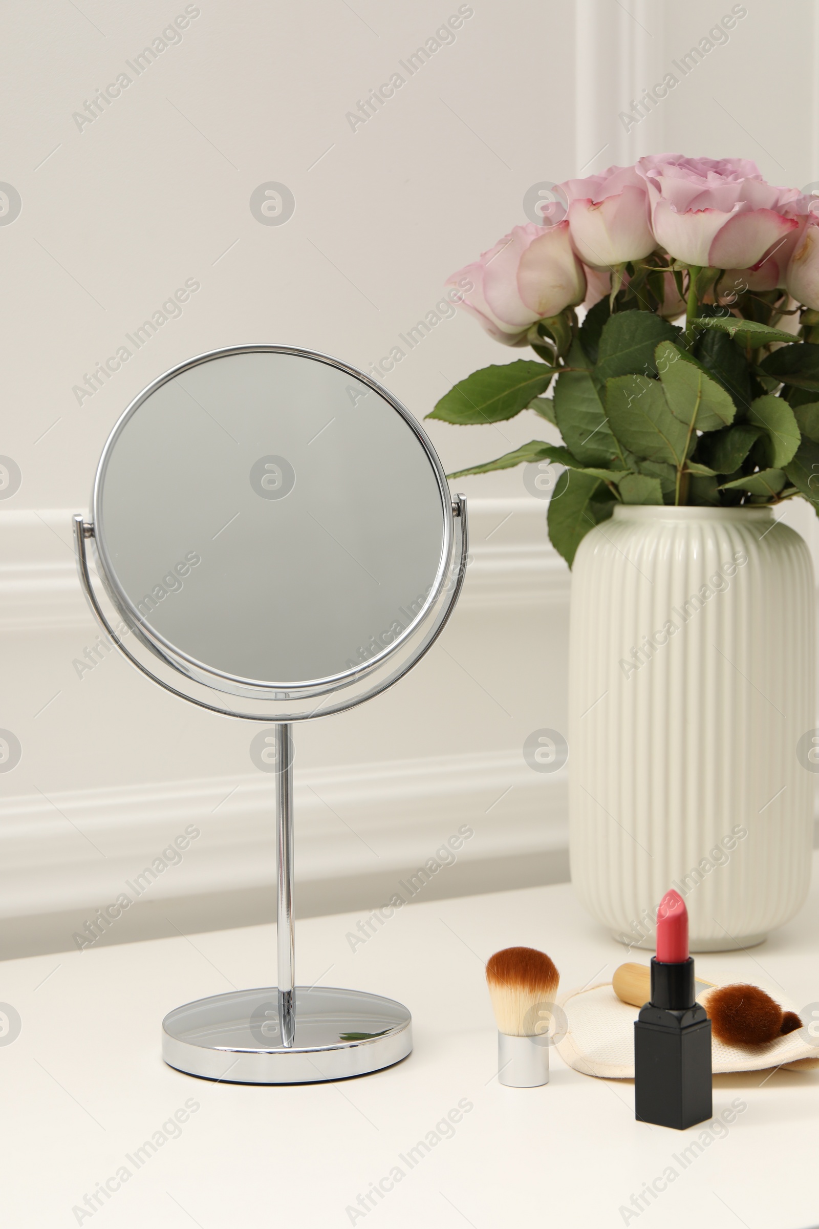 Photo of Mirror, cosmetic products and vase with pink roses on white dressing table