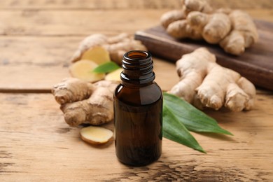 Glass bottle of essential oil and ginger root on wooden table