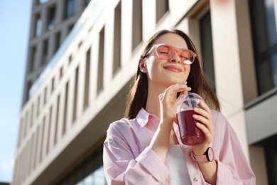 Photo of Young woman in sunglasses with plastic cup of fresh juice outdoors, low angle view. Space for text