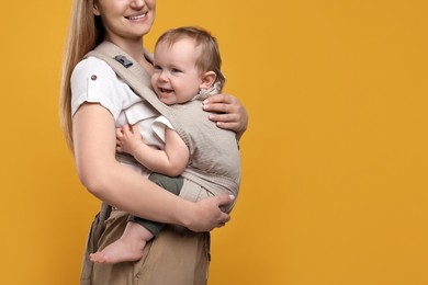 Photo of Mother holding her child in sling (baby carrier) on orange background, closeup. Space for text