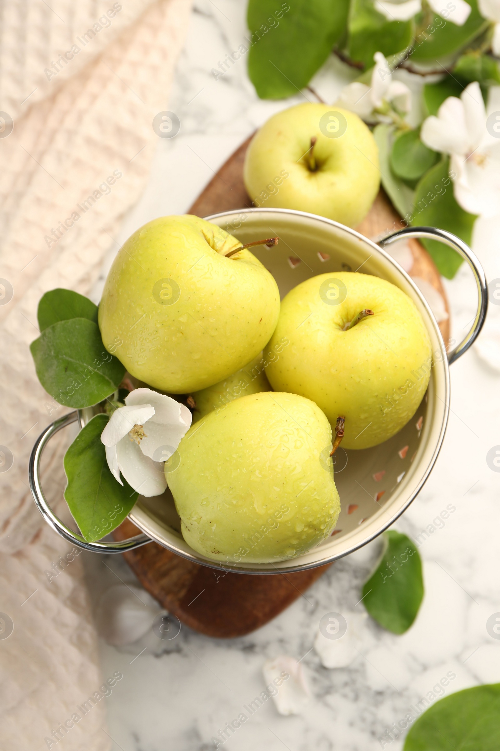 Photo of Colander with fresh apples and beautiful spring blossoms on white marble table, flat lay