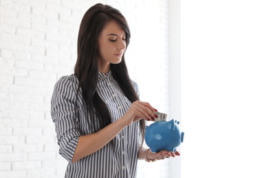 Photo of Woman putting money into piggy bank indoors, space for text