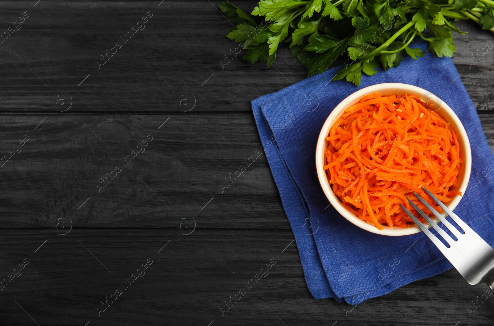 Photo of Delicious Korean carrot salad and parsley on black wooden table, flat lay. Space for text