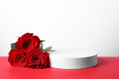 Photo of Stylish presentation for product. Round podium and beautiful roses on red table against white background, space for text