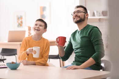 Photo of Little boy and his dad drinking tea together in kitchen