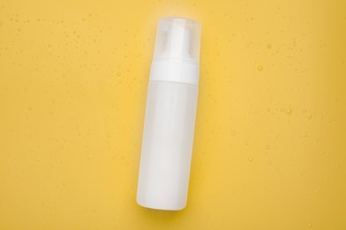 Photo of Wet bottle of face cleansing product on pale orange background, top view