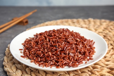 Plate with delicious cooked brown rice on grey table