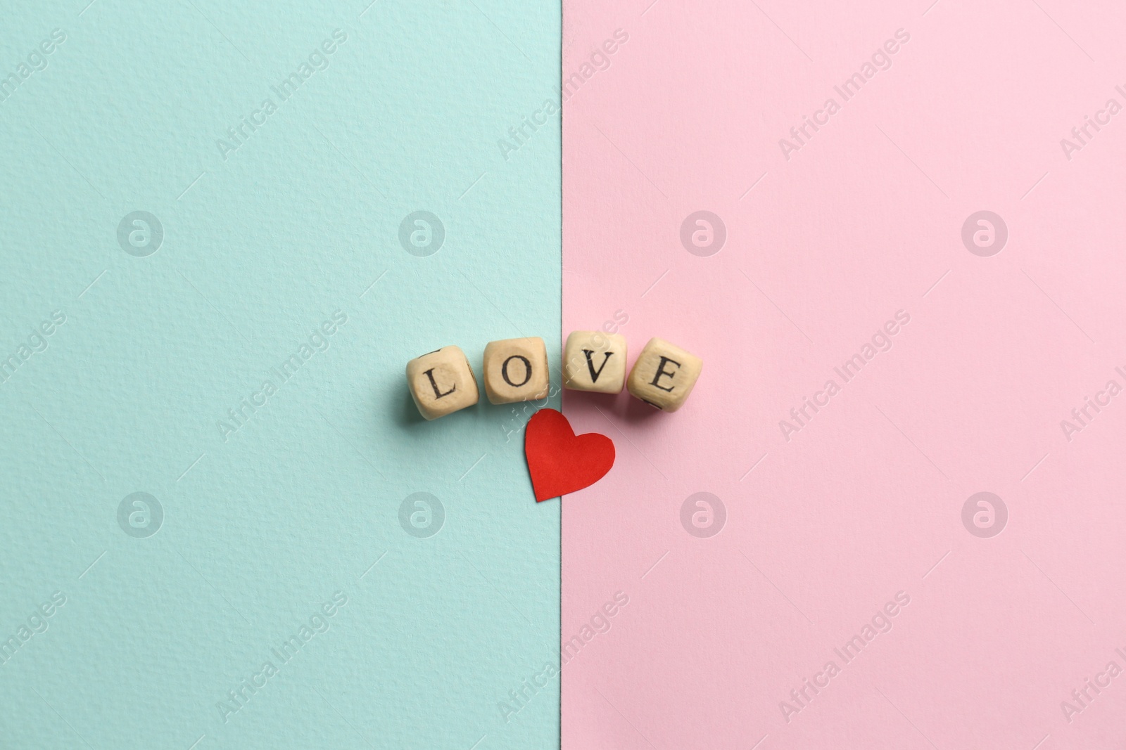 Photo of Word Love made of small wooden cubes with letters near red paper heart on color background, flat lay