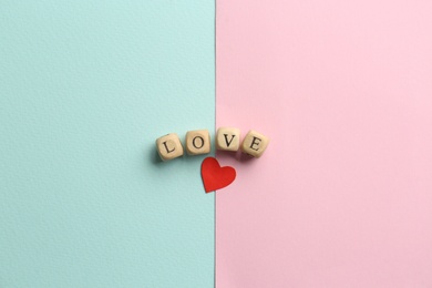 Photo of Word Love made of small wooden cubes with letters near red paper heart on color background, flat lay