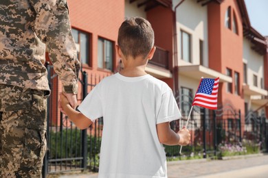 Photo of Soldier and his little son with American flag outdoors, back view. Veterans Day in USA