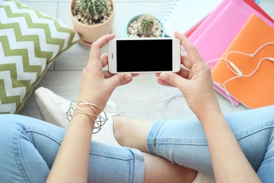 Photo of Young woman holding mobile phone with blank screen in hands, indoors