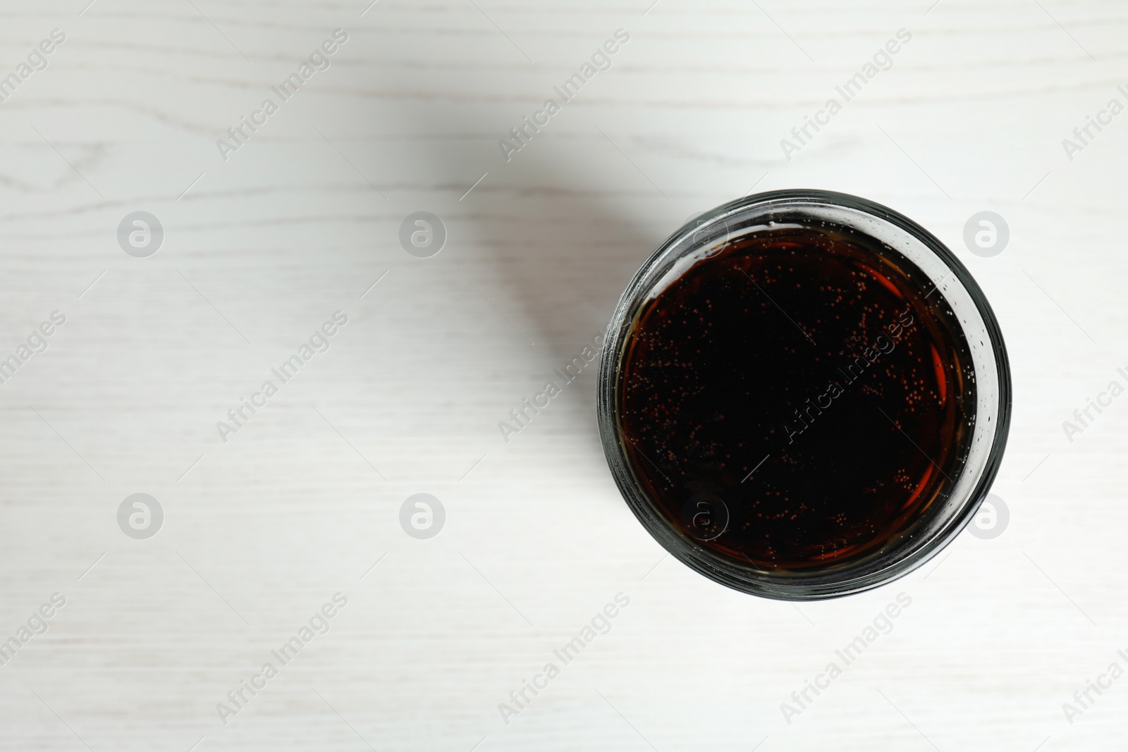 Photo of Glass of refreshing soda drink on white wooden background, top view. Space for text