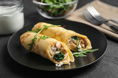 Photo of Delicious thin pancakes with chicken and mushrooms on black table