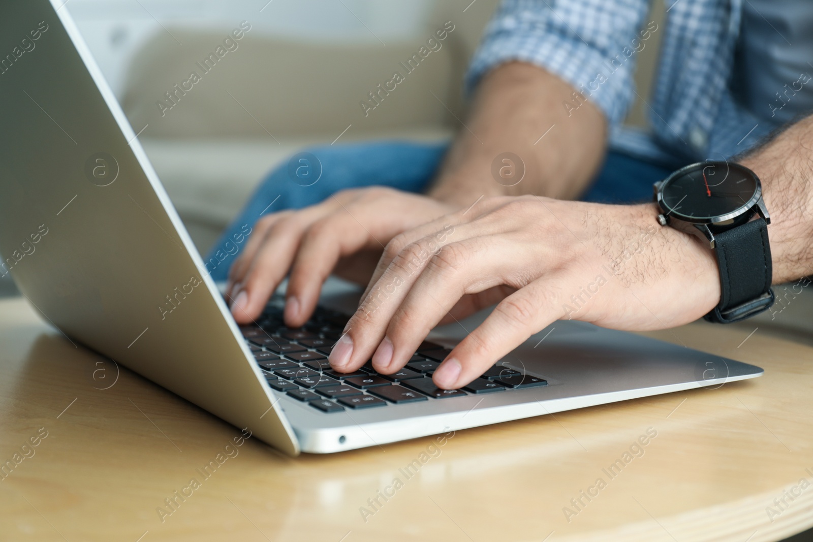Photo of Man working on modern laptop at wooden table indoors, closeup