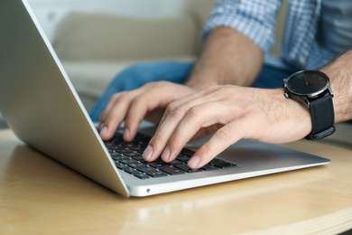 Man working on modern laptop at wooden table indoors, closeup