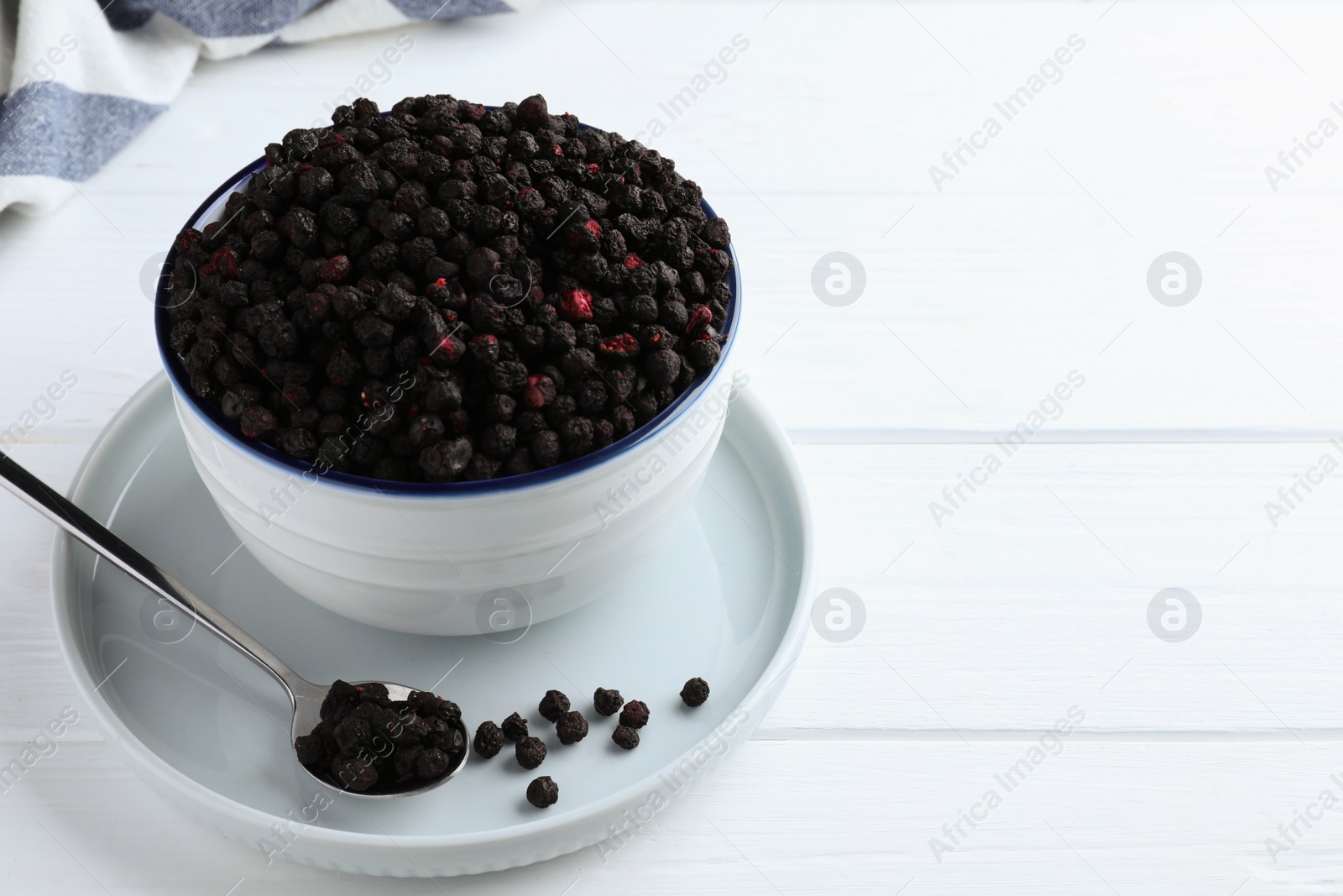 Photo of Bowl and spoon with dried blueberries on white wooden table. Space for text