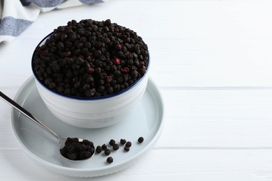 Photo of Bowl and spoon with dried blueberries on white wooden table. Space for text