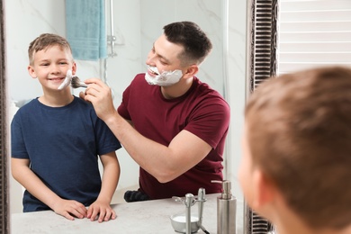 Photo of Dad applying shaving foam on son's face at mirror in bathroom