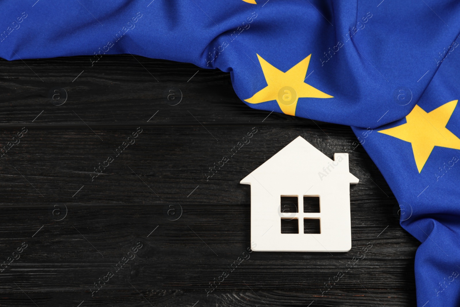 Photo of House model and flag of European Union on black wooden table, flat lay. Space for text