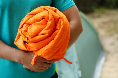 Photo of Man holding rolled sleeping bag outdoors, closeup