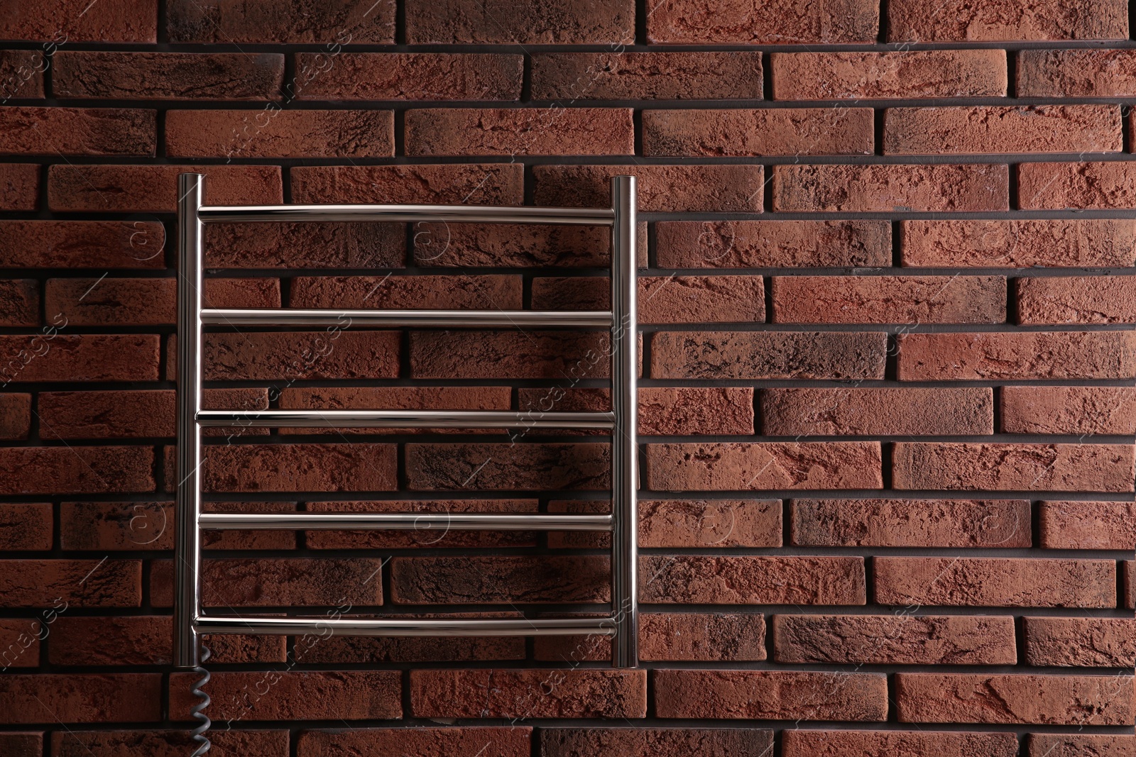 Photo of Modern heated towel rail on red brick wall. Space for text