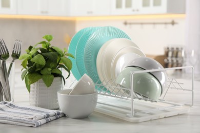 Many different clean dishware, cutlery and houseplant on white marble table in kitchen