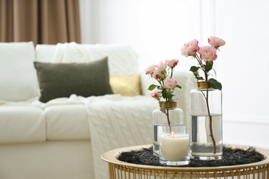Burning candle and vases with beautiful roses on table indoors, space for text. Interior elements