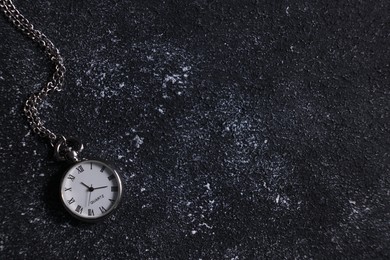 Photo of Silver pocket clock with chain on dark textured table, top view. Space for text