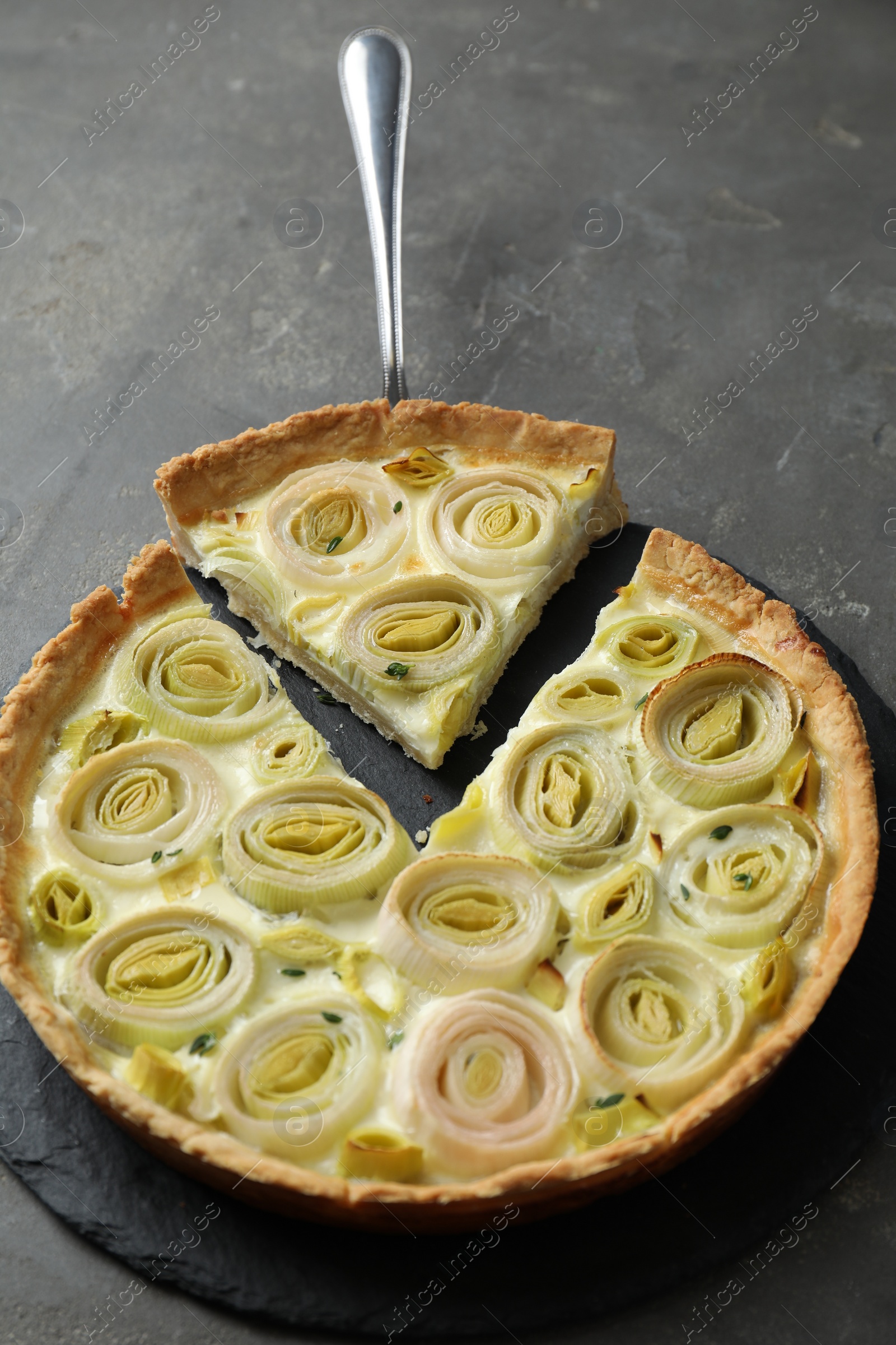 Photo of Tasty leek pie with cake server on dark textured table