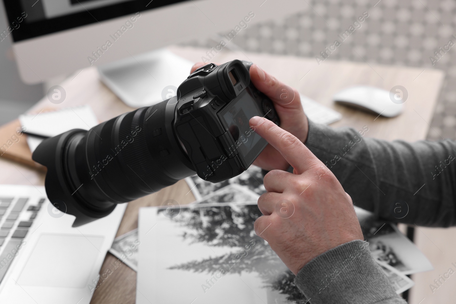 Photo of Professional photographer with digital camera at table indoors, closeup