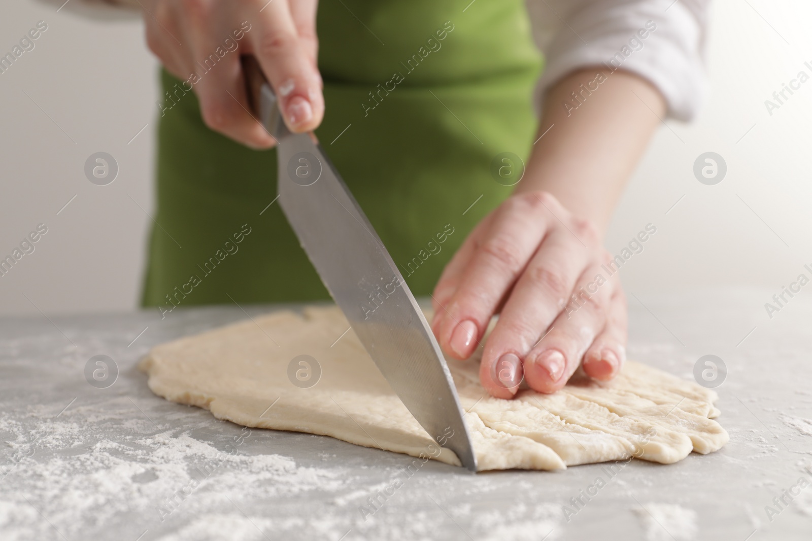 Photo of Woman cutting dough at light grey marble table, closeup. Cooking grissini