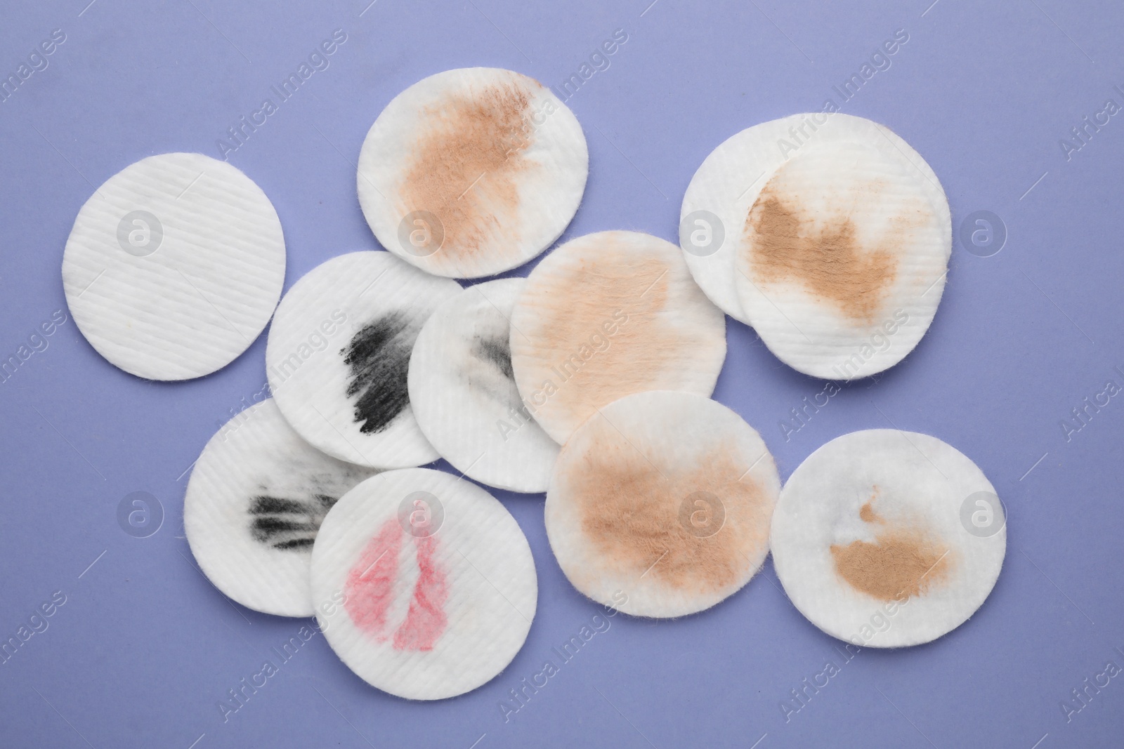 Photo of Clean and dirty cotton pads after removing makeup on light purple background, flat lay