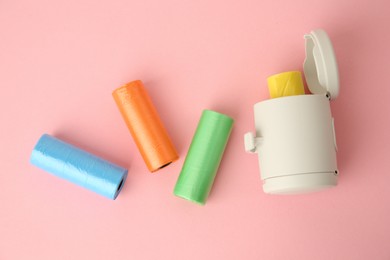 Photo of Dog waste bags and dispenser on pink background, flat lay