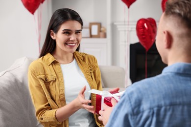 Photo of Woman receiving gift box from her boyfriend indoors. Valentine's day celebration.