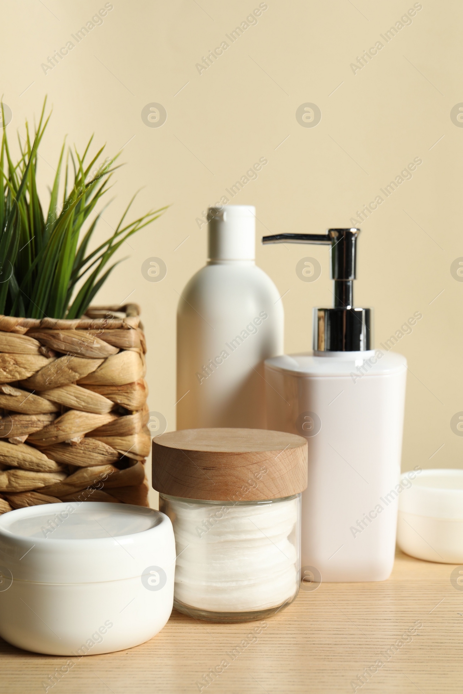 Photo of Different bath accessories and houseplant on wooden table against beige background, closeup