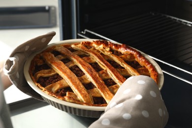 Woman taking delicious freshly baked meat pie from oven, closeup
