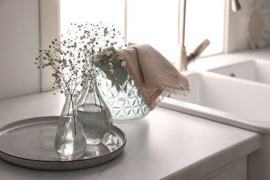 Photo of Vases with gypsophila flowers near sink in kitchen, space for text. Interior design