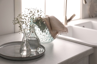 Vases with gypsophila flowers near sink in kitchen, space for text. Interior design