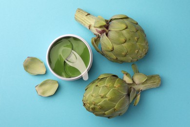 Photo of Package of under eye patches and artichokes on light blue background, flat lay. Cosmetic product