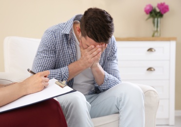 Depressed young man having appointment with psychologist in office