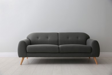 Photo of Comfortable grey sofa near white wall indoors. Interior design