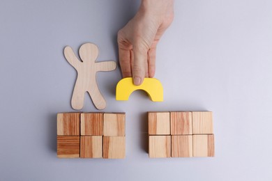 Photo of Woman putting wooden block to help human figure cross bridge on light grey background, top view. Connection, relationships, support and deal concepts