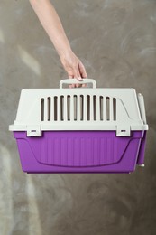 Photo of Woman holding violet pet carrier against grey wall, closeup