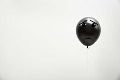 Black balloon with sad face on light grey background. Space for text