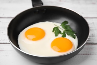 Tasty fried eggs with parsley in pan on white wooden table, closeup