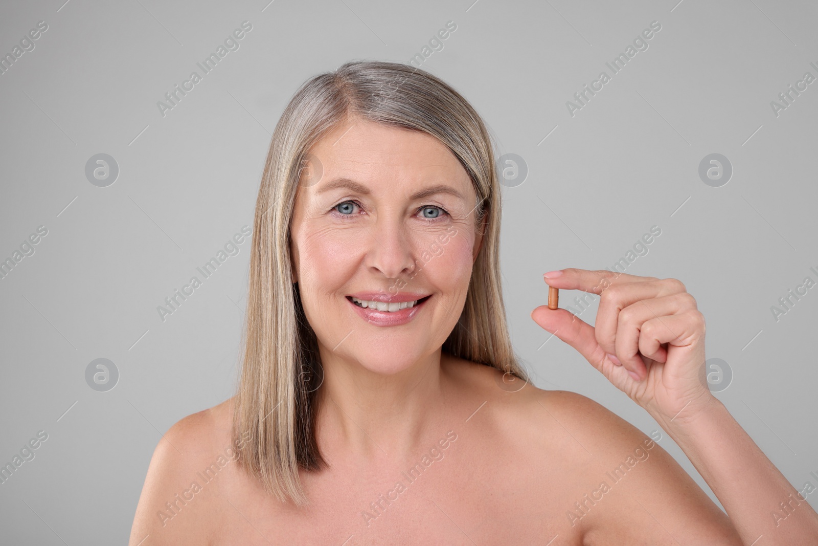 Photo of Beautiful woman with vitamin capsule on grey background