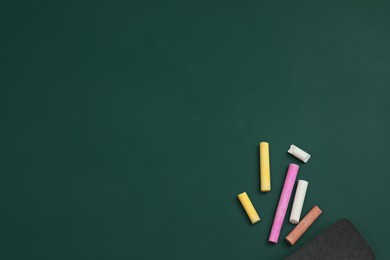 Photo of Colorful chalks and duster on green board, flat lay. Space for text
