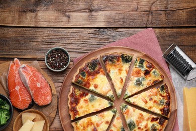 Photo of Delicious homemade quiche and ingredients on wooden table, flat lay